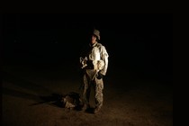 A photo of a man wearing camouflage, illuminated against a dark background