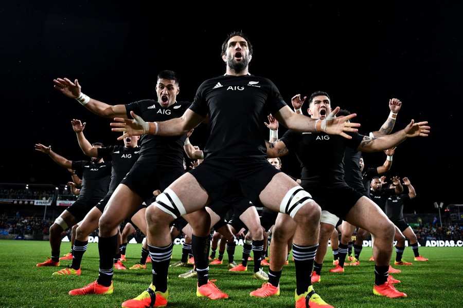 Members of the New Zealand All Blacks perform the haka on a playing field.
