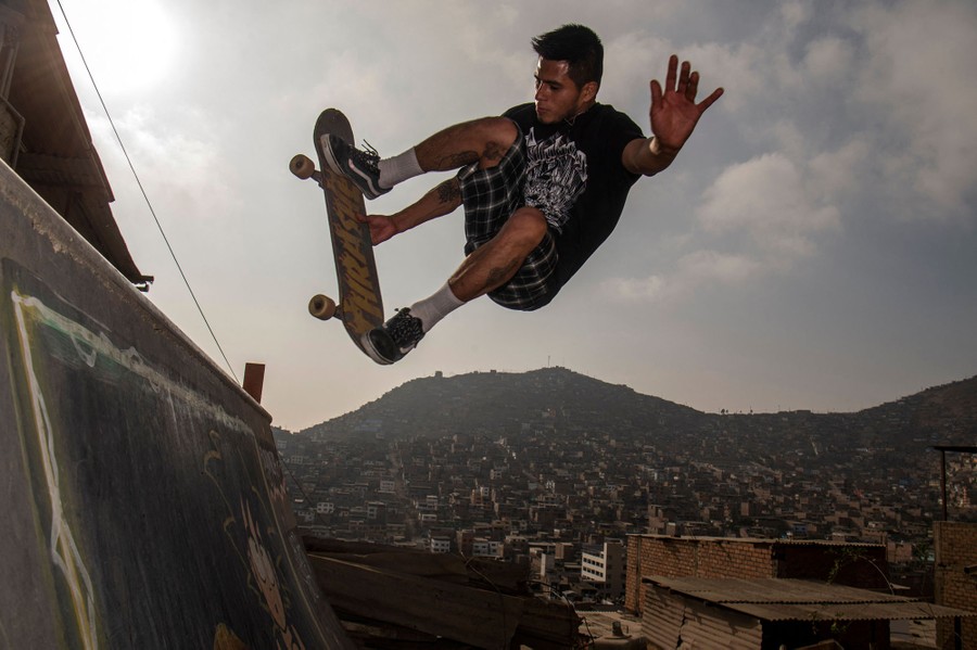 A skateboarder jumps off a ramp, with the hills of a city in the background.