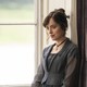 A scene from the film "Persuasion," depicting Dakota Johnson as Anne Elliott, sitting by a large window