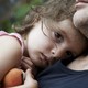 A tear streaks across sad child's nose as she rests her head on a man's chest.