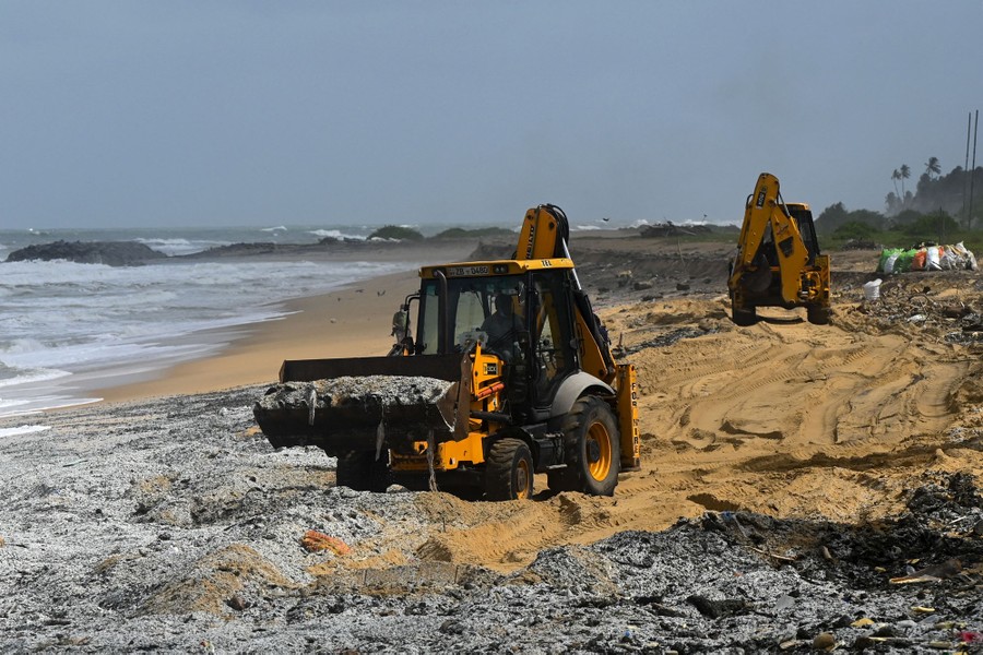 Two front-end loaders move debris and sand on a polluted beach.