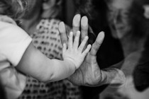 A little girl presses her hand to an old woman's through a glass window