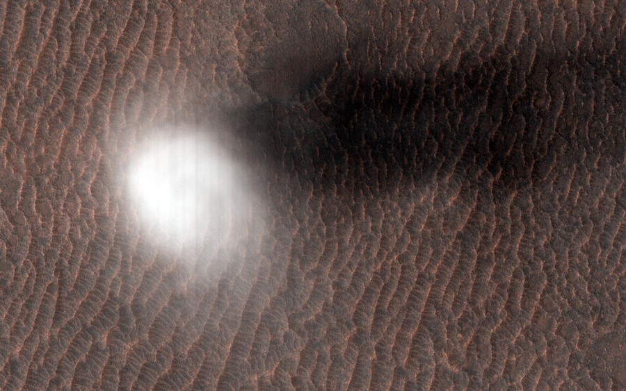 A plume of dust and a shadow are seen on the Martian surface.