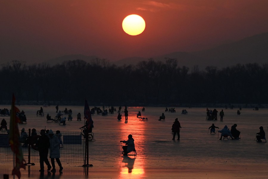 People ride sleds on a frozen lake at sunset.