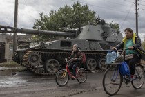 Balakliia residents riding bikes in front of a tank