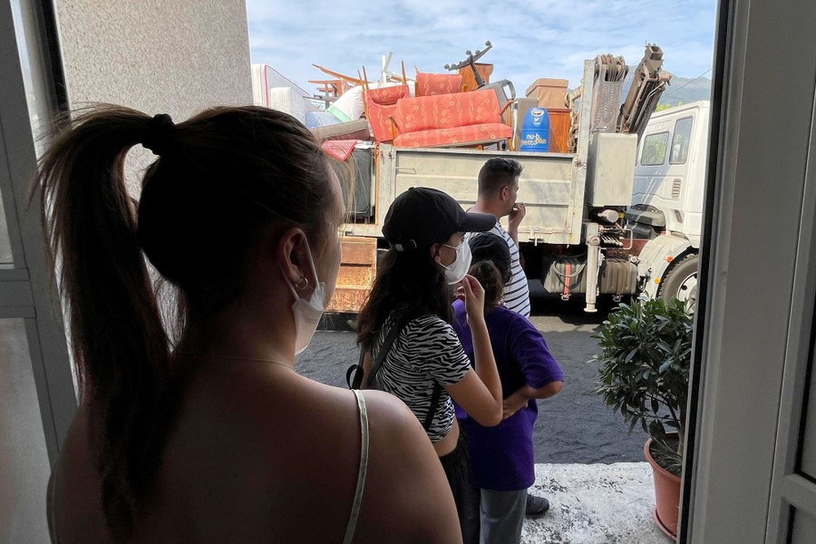 Several people stand in a doorway, beyond them is a truck filled with furniture in a street.