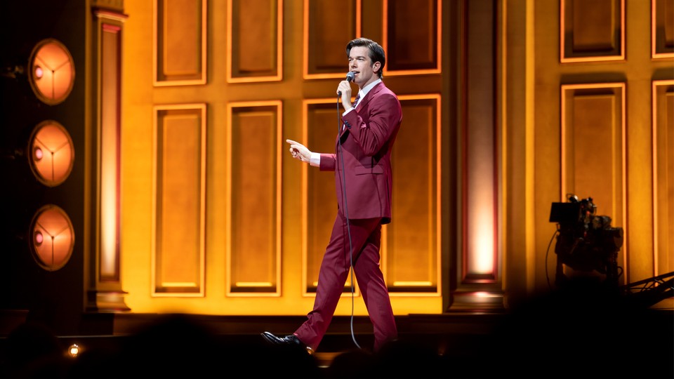 The comedian John Mulaney onstage with a microphone in his hand