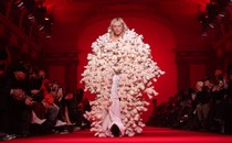 A model wearing a long coat made of stuffed animals walks down a runway.