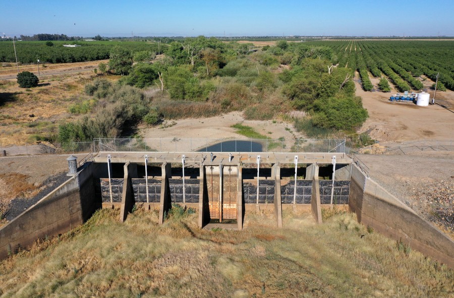 Dam floodgates stand in a dry landscape, among farm fields.