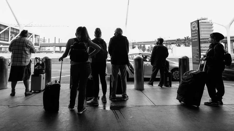 A black and white photo of travelers with suitcases wearing masks