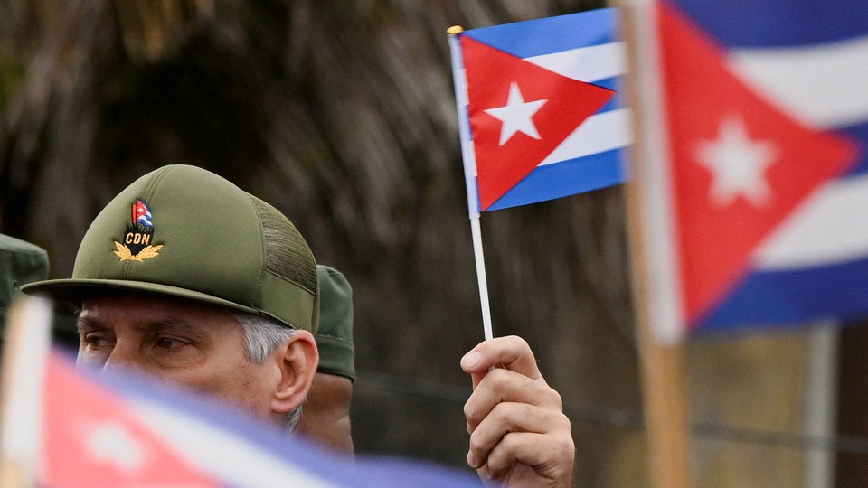 A man in a CDN cap holds a Cuban flag