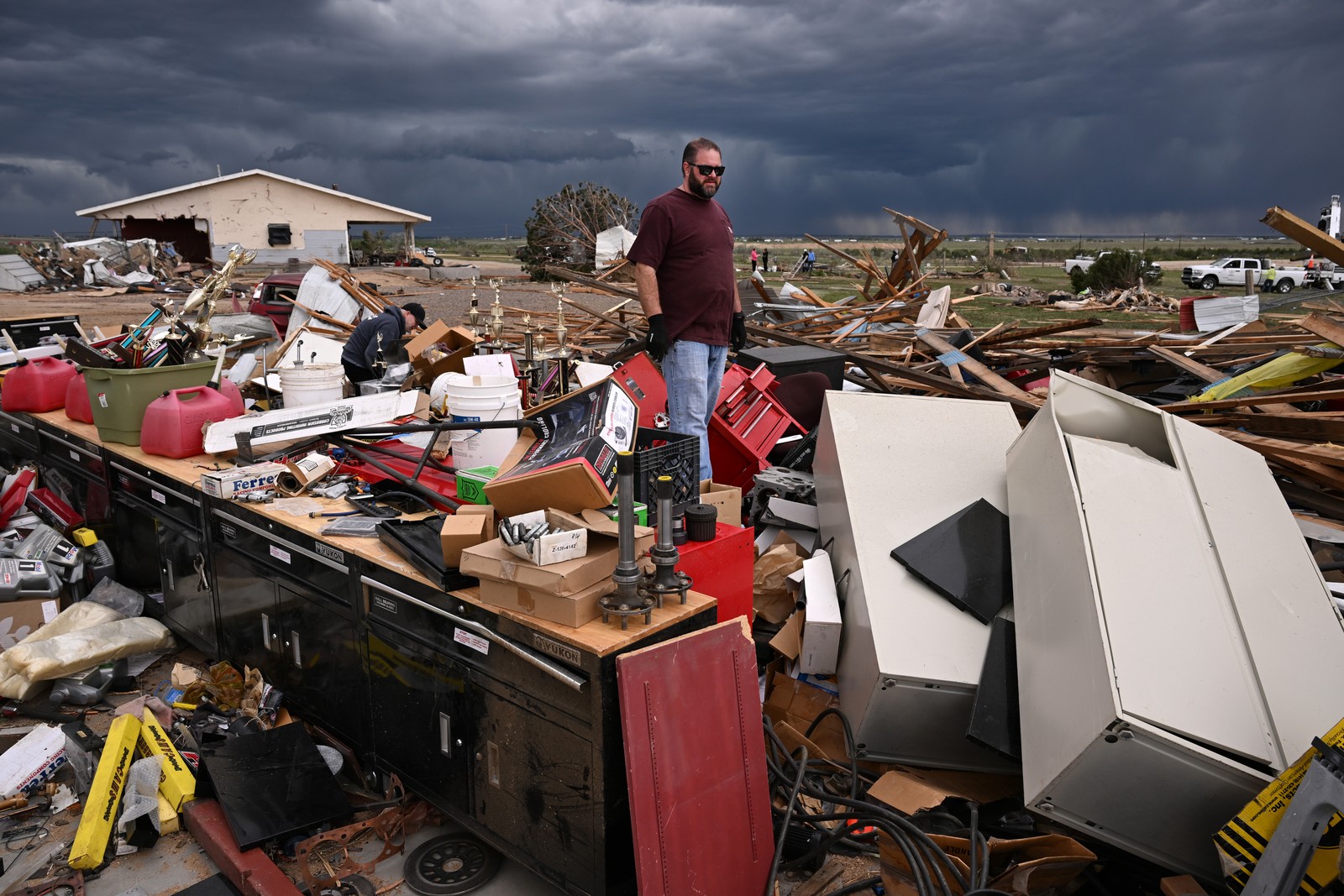 A man stands in the middle of a broad field of debris left after a tornado destroyed a house.