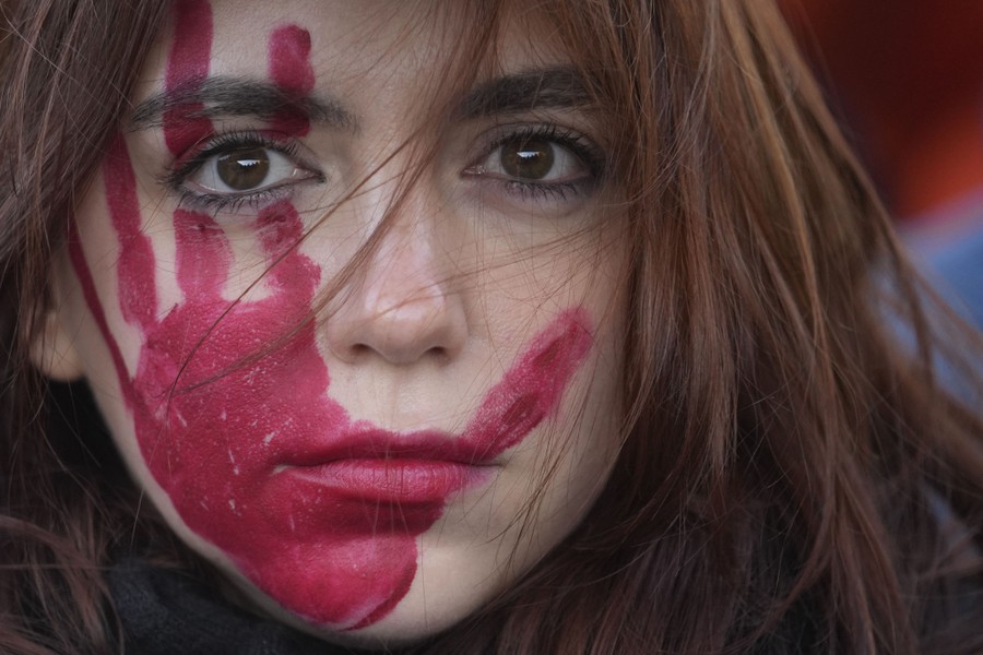 A close view of a woman's face, mostly covered by a red handprint made with makeup, during a protest