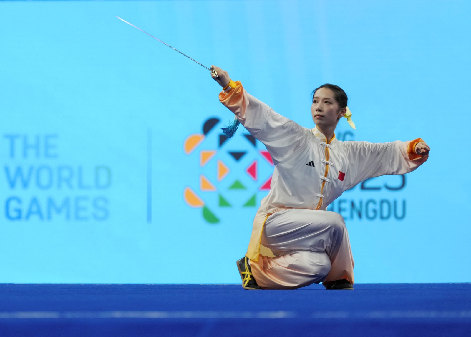 A martial artist crouches while holding a sword during a competition.