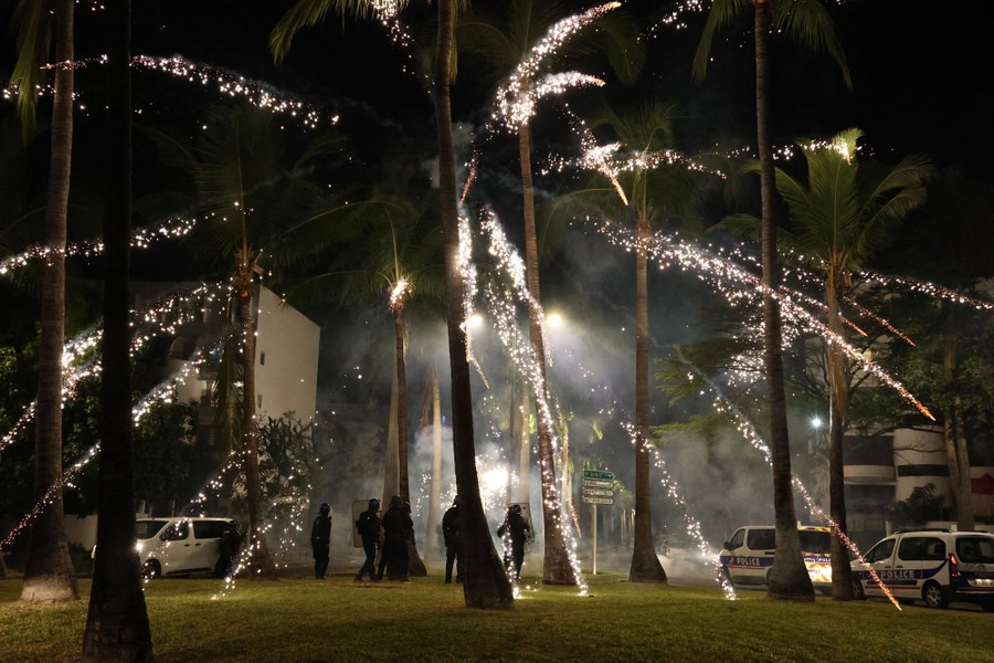 A firework explodes above a group of riot police officers.