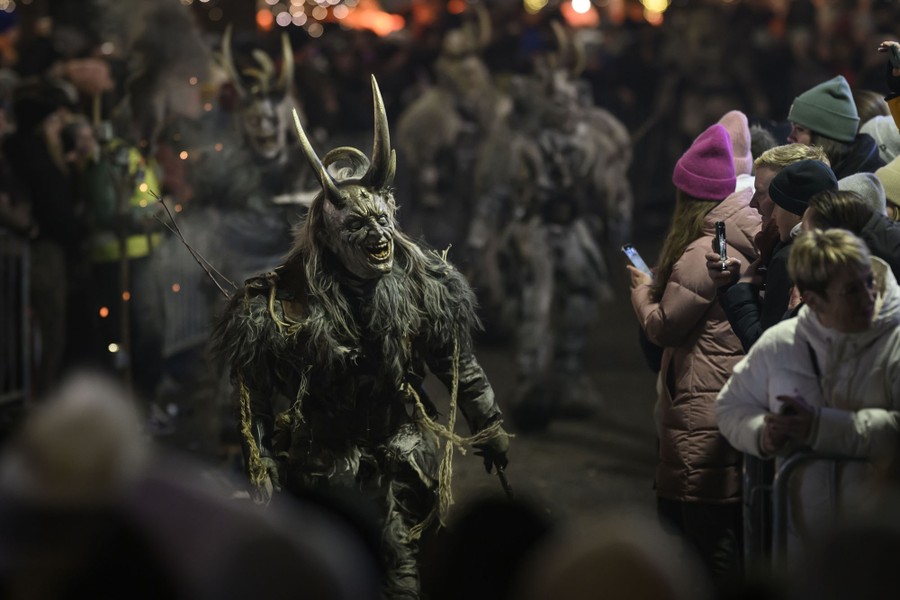 A crowd watches as performers in frightening demonlike costumes parade past.
