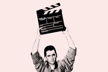 A photo of John Cusack holding a clapperboard above his head