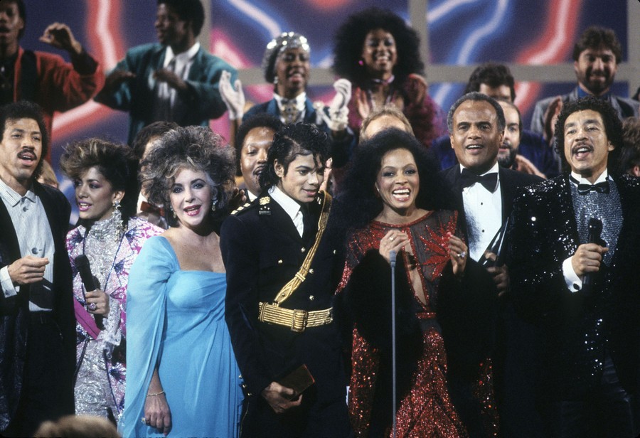 Lionel Richie, Sheila E., Elizabeth Taylor, Michael Jackson, Diana Ross, Harry Belafonte, and Smokey Robinson sing together on stage.