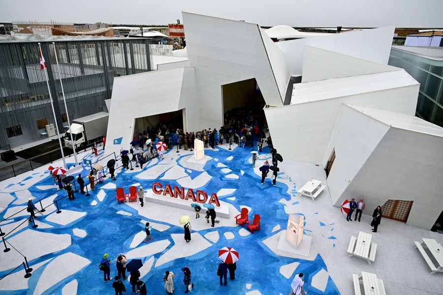 An elevated view of an angular building with a crowd waiting to enter and a large sign outside reading "Canada"