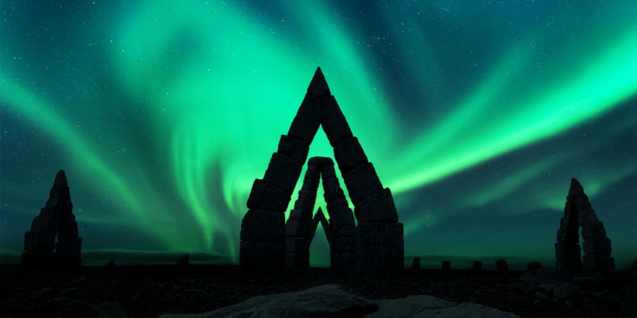 The Northern Lights fill the night sky above several stone arches.