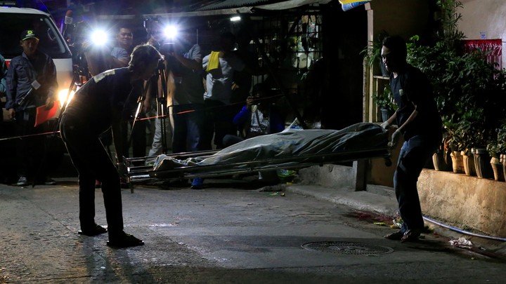 Funeral workers use a stretcher to carry the body of a suspected drug pusher.
