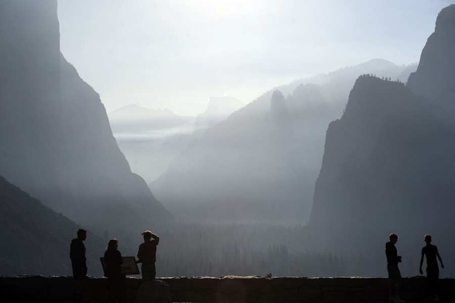 Several people look out to a view of a steep mountain canyon, the air hazy with smoke.