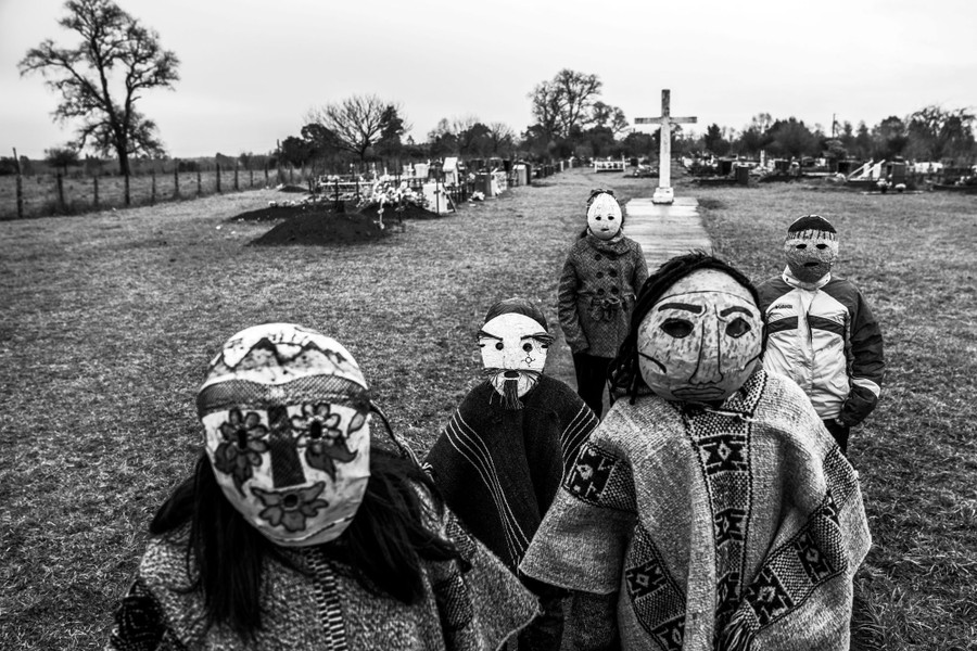 Five children wear traditional masks while standing in a cemetery.