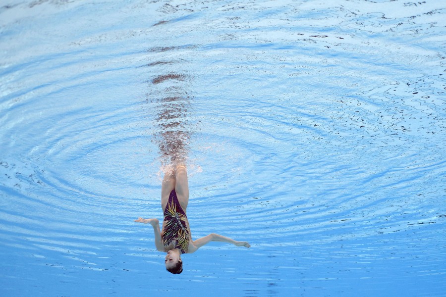 An artistic swimmer is underwater, upside down, during a performance.