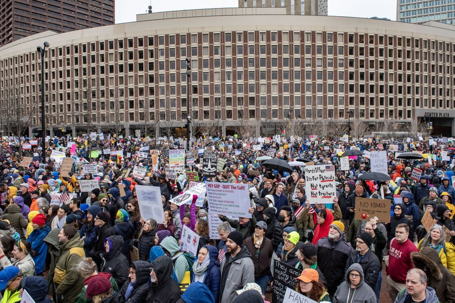 A large crowd of protesters stands near a wide city building.
