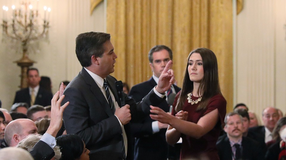 A White House intern reaches for the microphone held by CNN correspondent Jim Acosta.