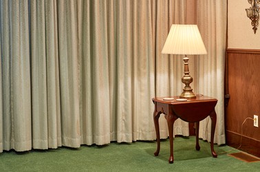 A lamp on a table in a corner of a funeral parlor room
