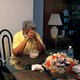 A woman sits at a table in her apartment, praying
