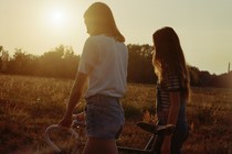 Two friends walking with a bike in a field