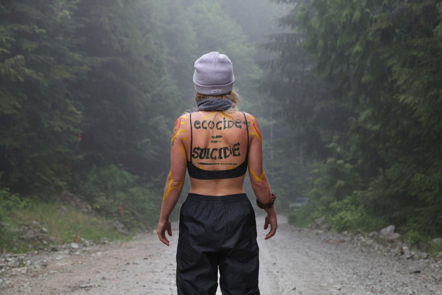 A woman stands on a dirt road with the words "Ecocide = Suicide" written across her back.