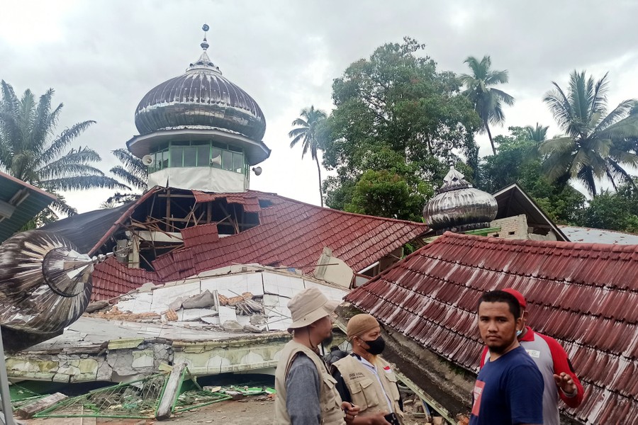 Several people stand beside the wreckage of a mosque that was damaged during an earthquake.
