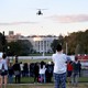 A helicopter flies over the White House as a crowd looks on