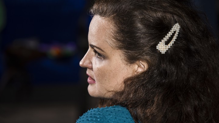 A woman with dark hair and a white hair clip watches a screen off-camera