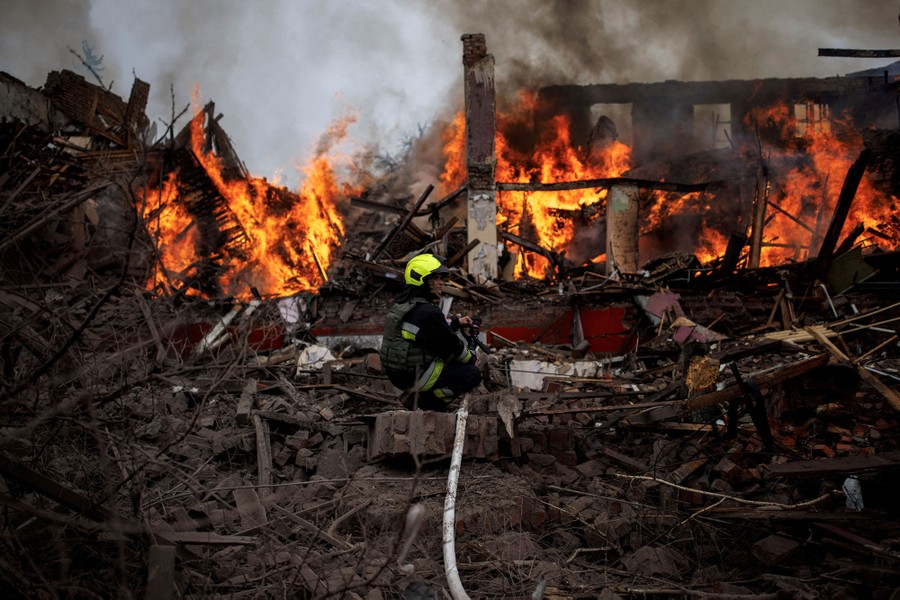 A firefighter holds a hose next to a burning building.