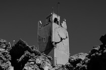 Black-and-white photograph of the cracked minaret of a mosque surrounded by rubble