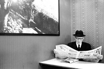 An elderly man wearing a hat and glasses reading a newspaper