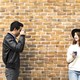 A man takes a photo of a woman against a brick wall.