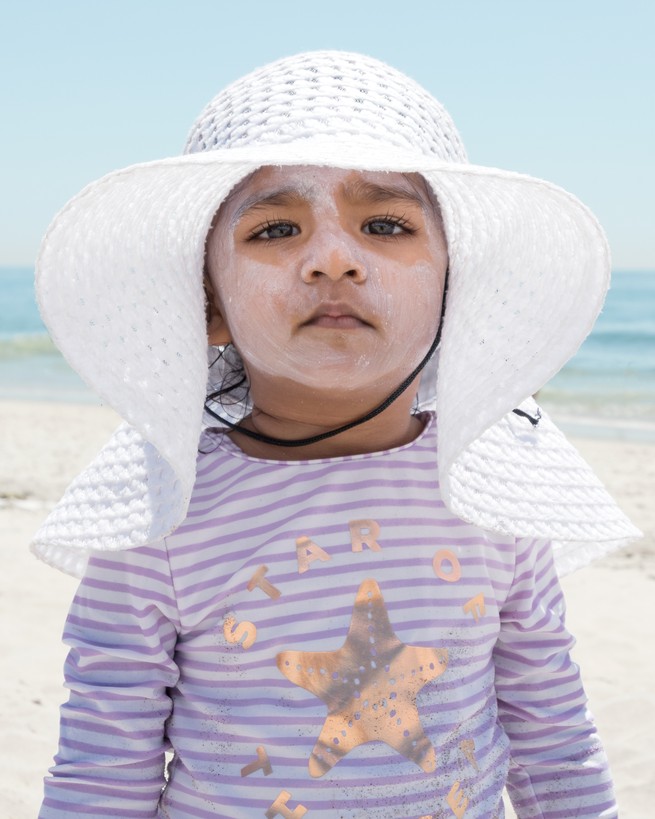 A child in a white hat with lots of sunscreen on her face