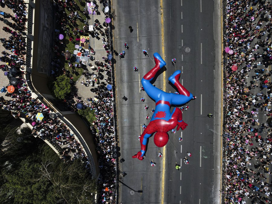 A top-down aerial view of a large Spider-Man balloon being pulled along a parade route.