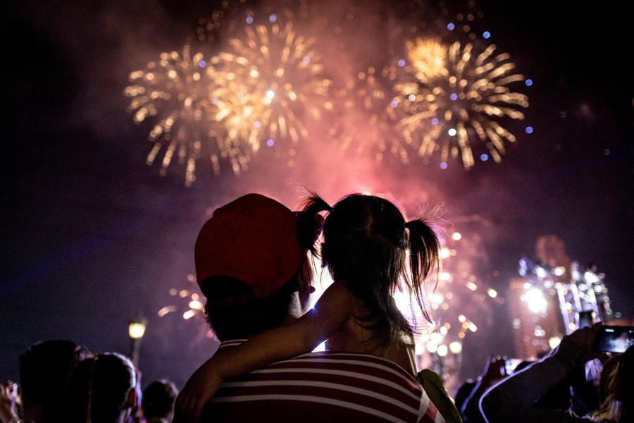 A man holds his child as both watch fireworks.
