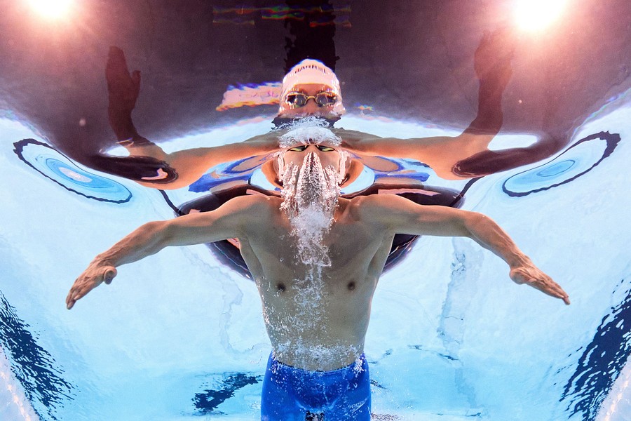 An underwater view of a swimmer passing overhead during a race, with many reflections and bubbles