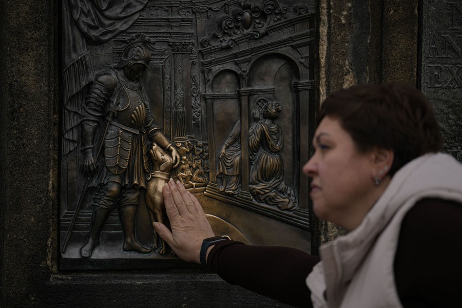 A person places their hand on a bronze plaque, touching a depiction of a dog, which has been rubbed clean by many hands.