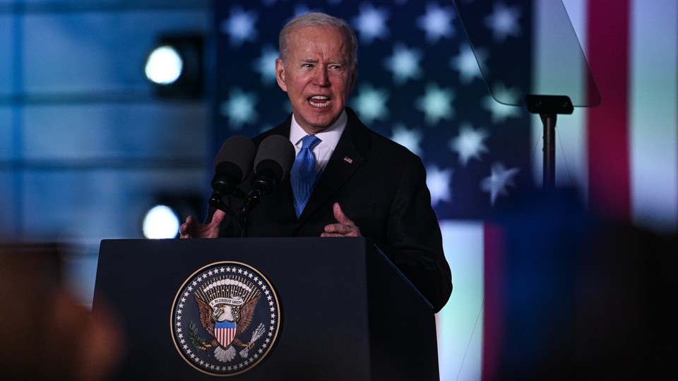 Biden with an animated expression giving a speech in front of a flag
