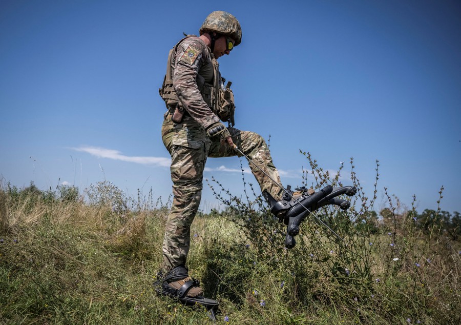 A soldier walks in a field, wearing unusual gear strapped to his feet, each "boot" having four short legs.