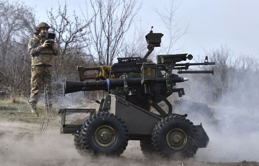 A soldier pilots a ground-based drone—a small four-wheeled vehicle mounted with several weapons.